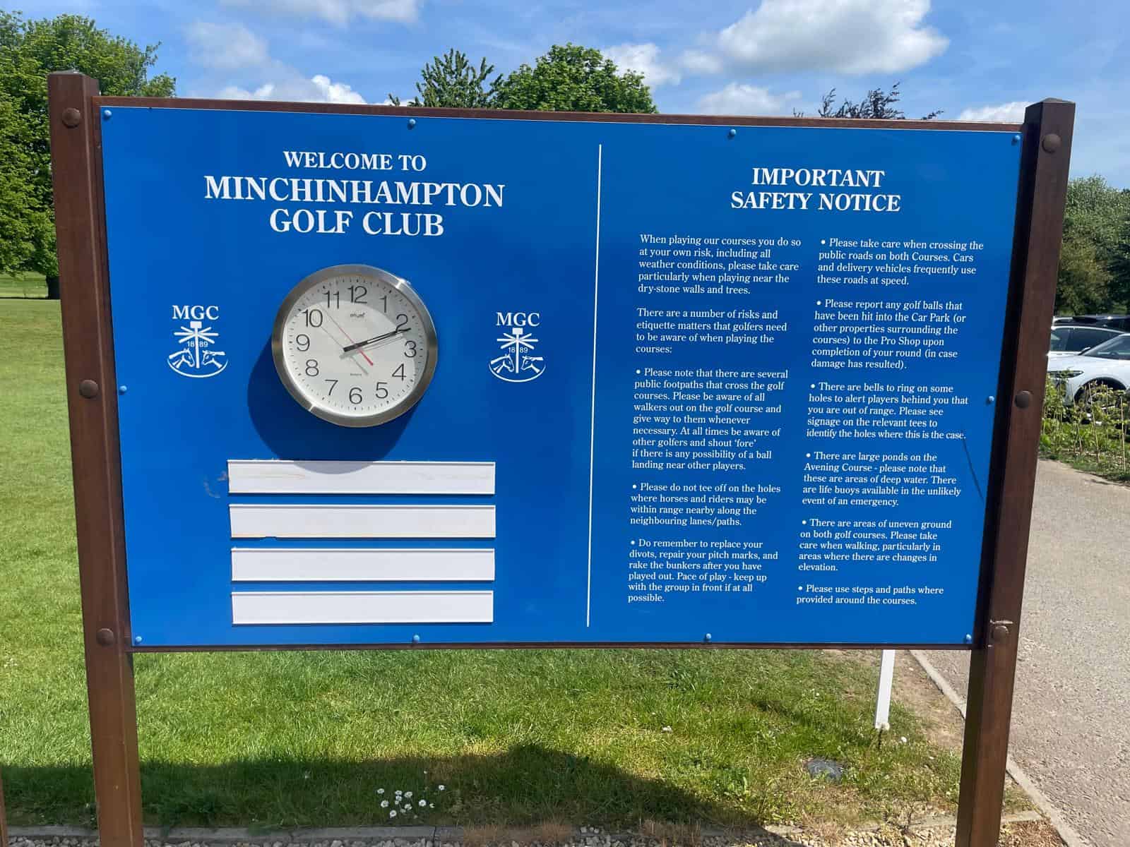 Blue Minchinhampton Golf Club welcome board featuring the club clock, logo and course safety information.